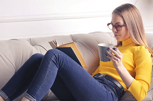 Woman reading a book sitting on a couch and holding a mug